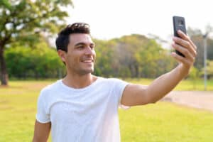 Happy young handsome Hispanic man taking selfie at the park → Social Kings Grow your following